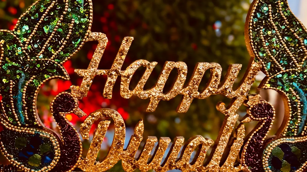 A glittering Happy Diwali sign decorated with peacock designs on a table