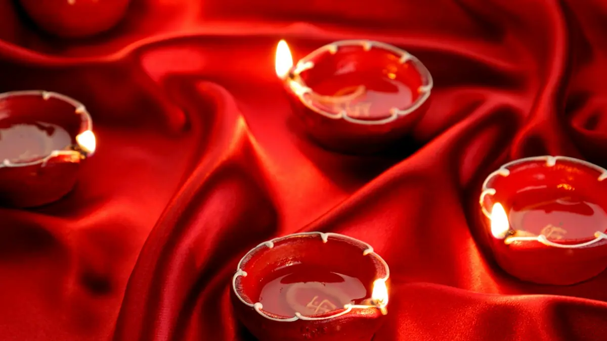 Small lit glass diya candle holders arranged on red silk fabric