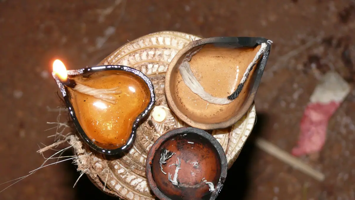 Three handmade clay oil lamps, one of them lit, on a wooden surface