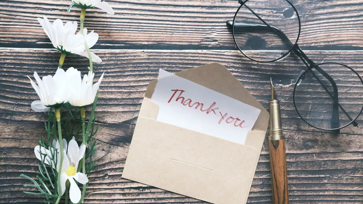 A handwritten thank-you note in an envelope beside a pair of glasses and flowers