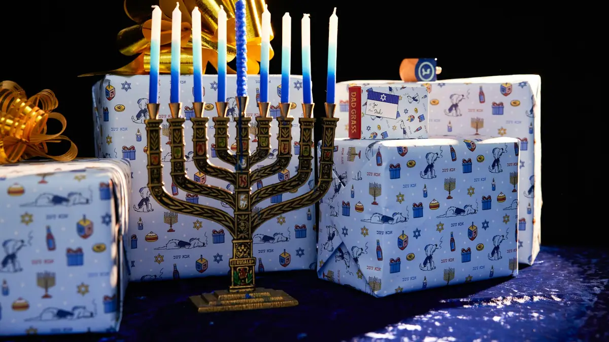 A lit Hanukkah menorah in front of blue and white wrapped gifts