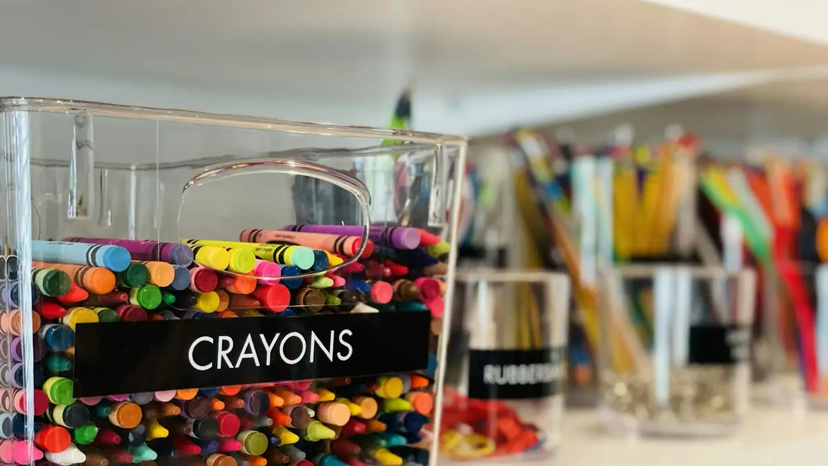 A classroom shelf with a clear bin of colorful crayons