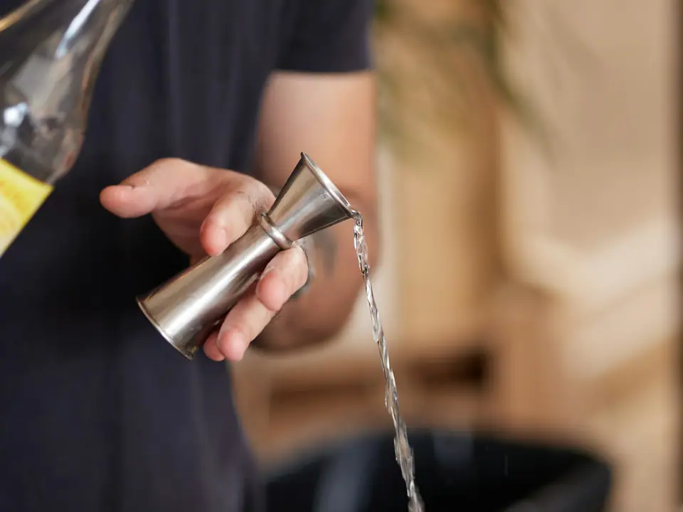 Pouring a drink into a metal jigger for a cocktail