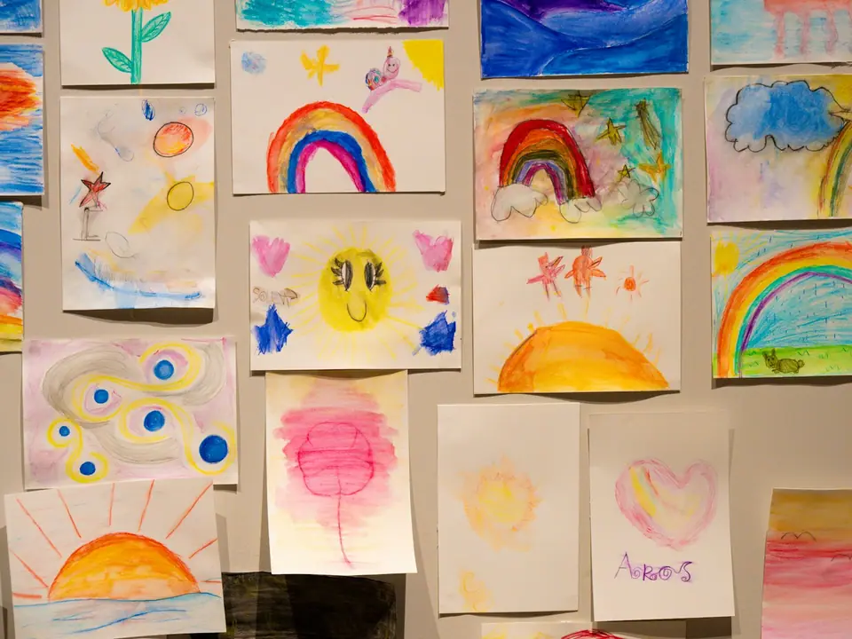Colorful children's drawings of rainbows, suns and flowers pinned to a wall