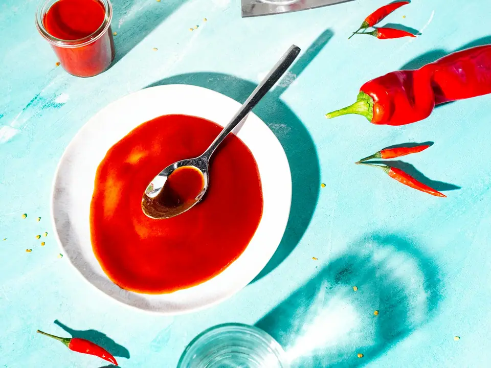 A bowl of red chili sauce surrounded by fresh chilies