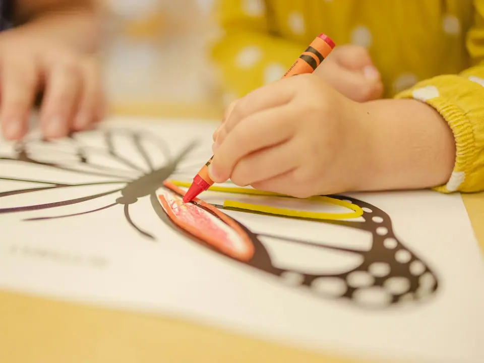 A child coloring a butterfly drawing with a red crayon