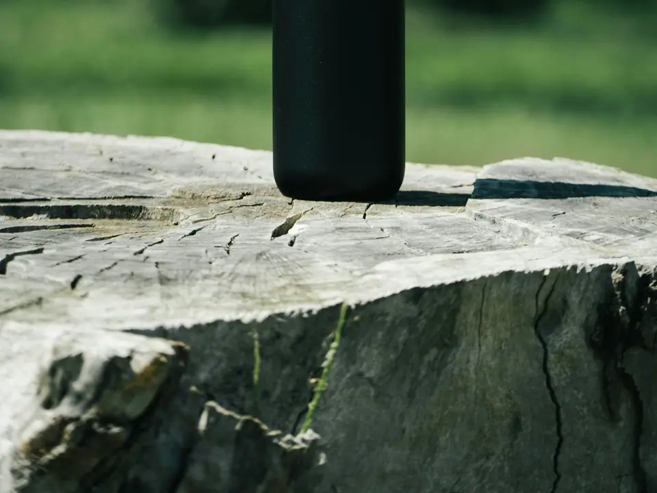 A plain black water bottle on a rustic wooden surface