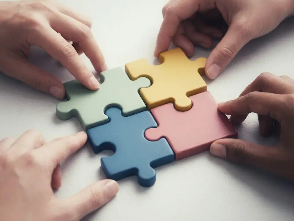 Hands fitting four large jigsaw puzzle pieces together