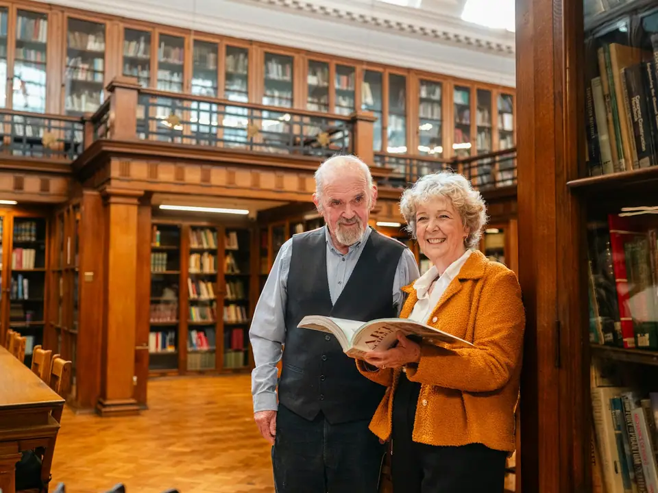 An older couple smiling and holding an open book in a library