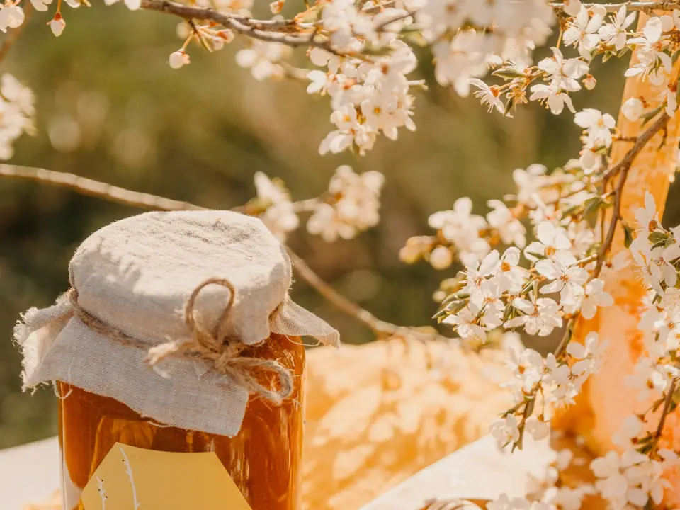 A jar of honey with a cloth lid beside spring blossoms