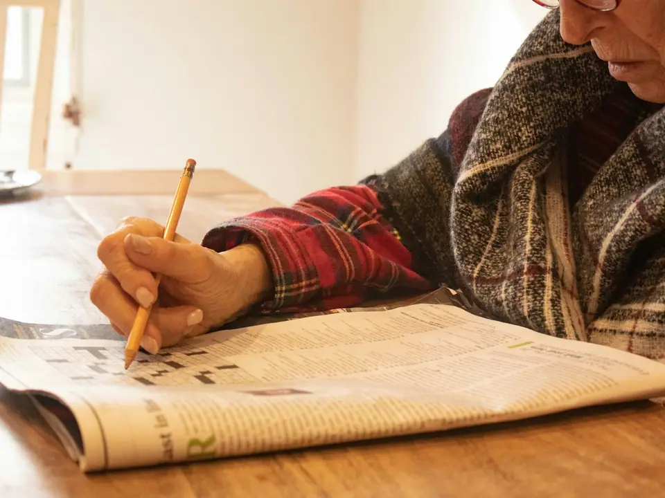 An older person's hand writing with a pencil at a table