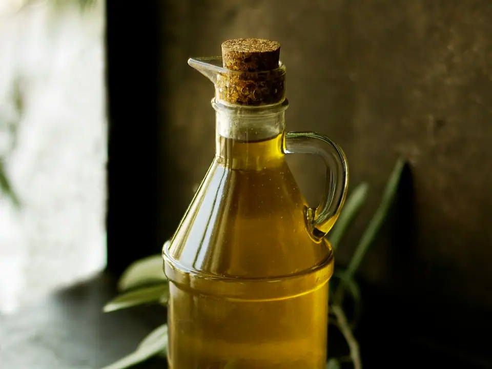 A glass cruet of golden olive oil beside olives