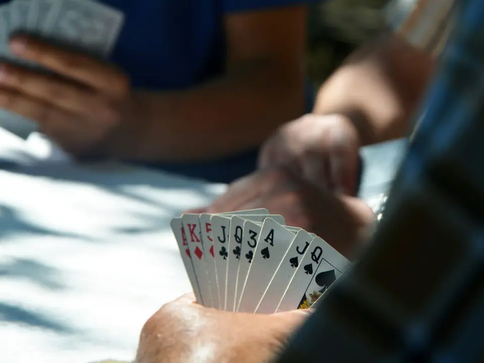 A group of friends holding playing cards around a table