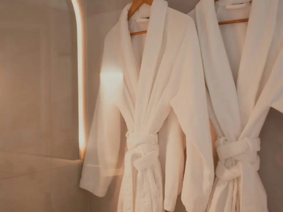 Two soft white bathrobes hanging on hooks
