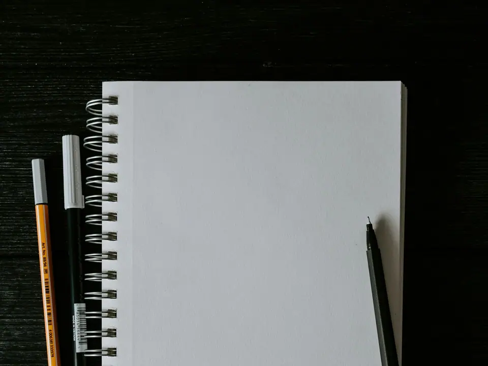 A blank spiral sketchbook with pens beside it