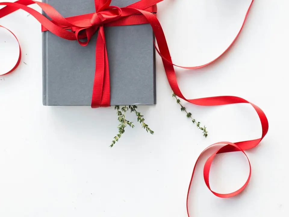 A gray hardcover book tied with a red ribbon beside a tealight candle