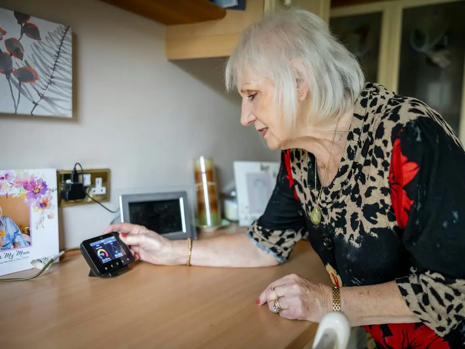 An older woman using a small screen propped up on her kitchen counter